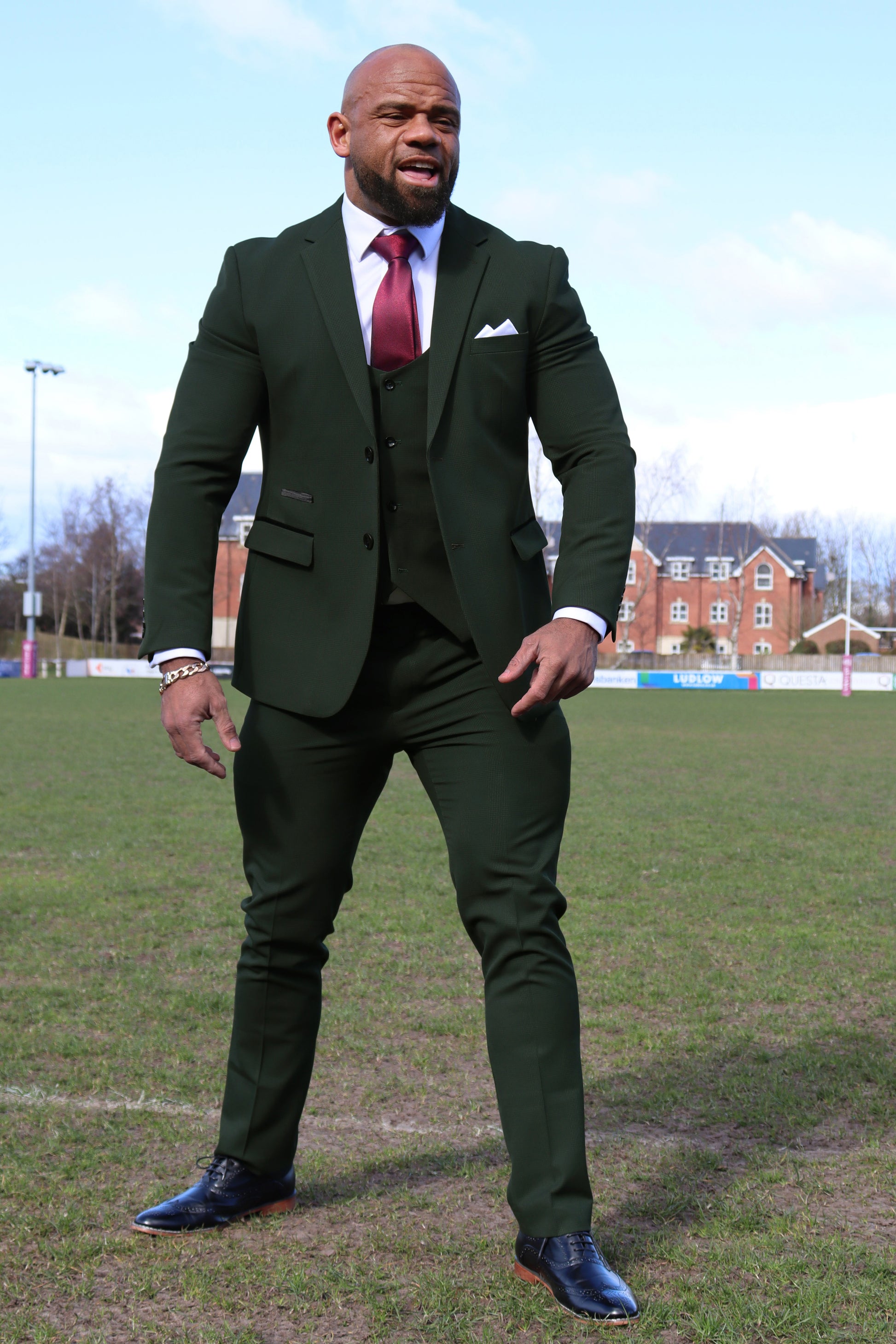 Man wearing the SUITBAE Charles Green Three-Piece Suit, featuring a dark green textured blazer, horseshoe-cut waistcoat, and slim trousers. Styled with a white shirt, burgundy tie, and black brogues — tailored for a muscular or plus-size build, combining structure, stretch, and sophistication.