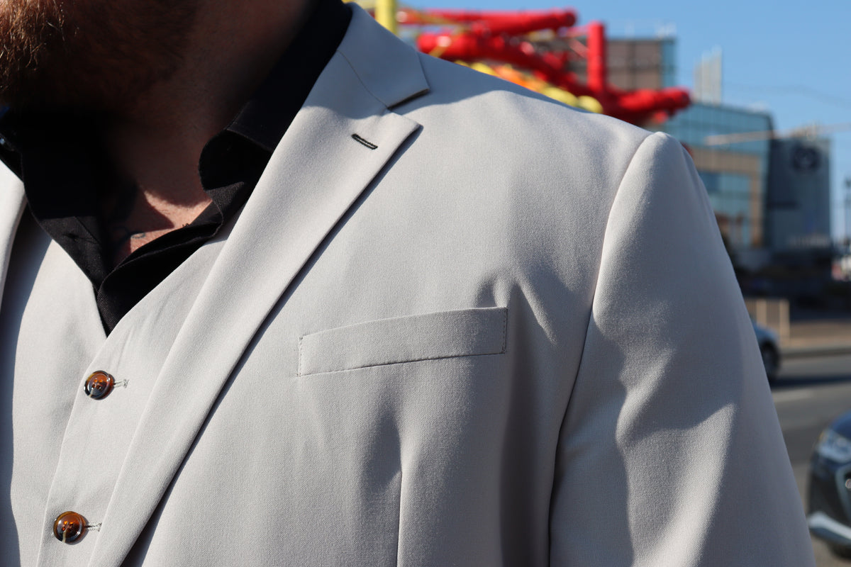 Close-up of the SUITBAE Kian Stone Three-Piece Suit — textured stone beige fabric with natural stretch and brown button detailing. A stylish plus-size suit that balances structure with comfort.
