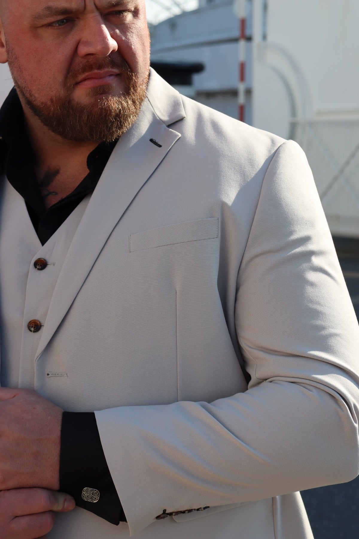 Close-up of the SUITBAE Kian Stone Three-Piece Suit — showing the textured stone beige fabric, brown buttons, and contrasting black shirt and cufflinks. A perfect plus-size option for weddings and summer formal events.