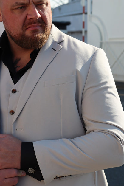 Close-up of the SUITBAE Kian Stone Three-Piece Suit — showing the textured stone beige fabric, brown buttons, and contrasting black shirt and cufflinks. A perfect plus-size option for weddings and summer formal events.