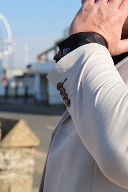 Close-up of the SUITBAE Kian Stone Three-Piece Suit — showing the textured stone beige fabric, brown button detailing, and black cufflink shirt contrast. Available in plus sizes for weddings and summer occasions.