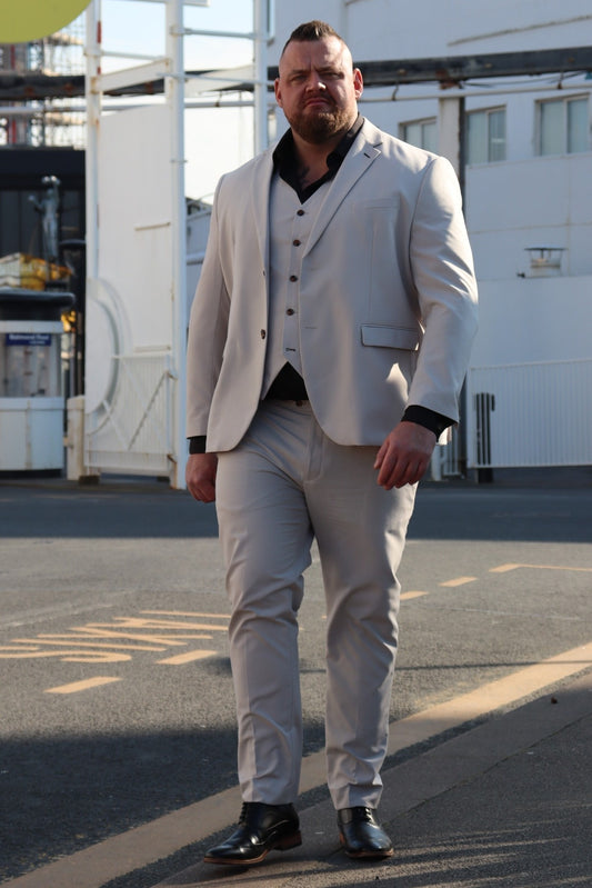 Model wearing the SUITBAE Kian Stone Three-Piece Suit — lightweight stone beige design with brown buttons and black shirt contrast, available in plus sizes, perfect for weddings, summer events and formal occasions.