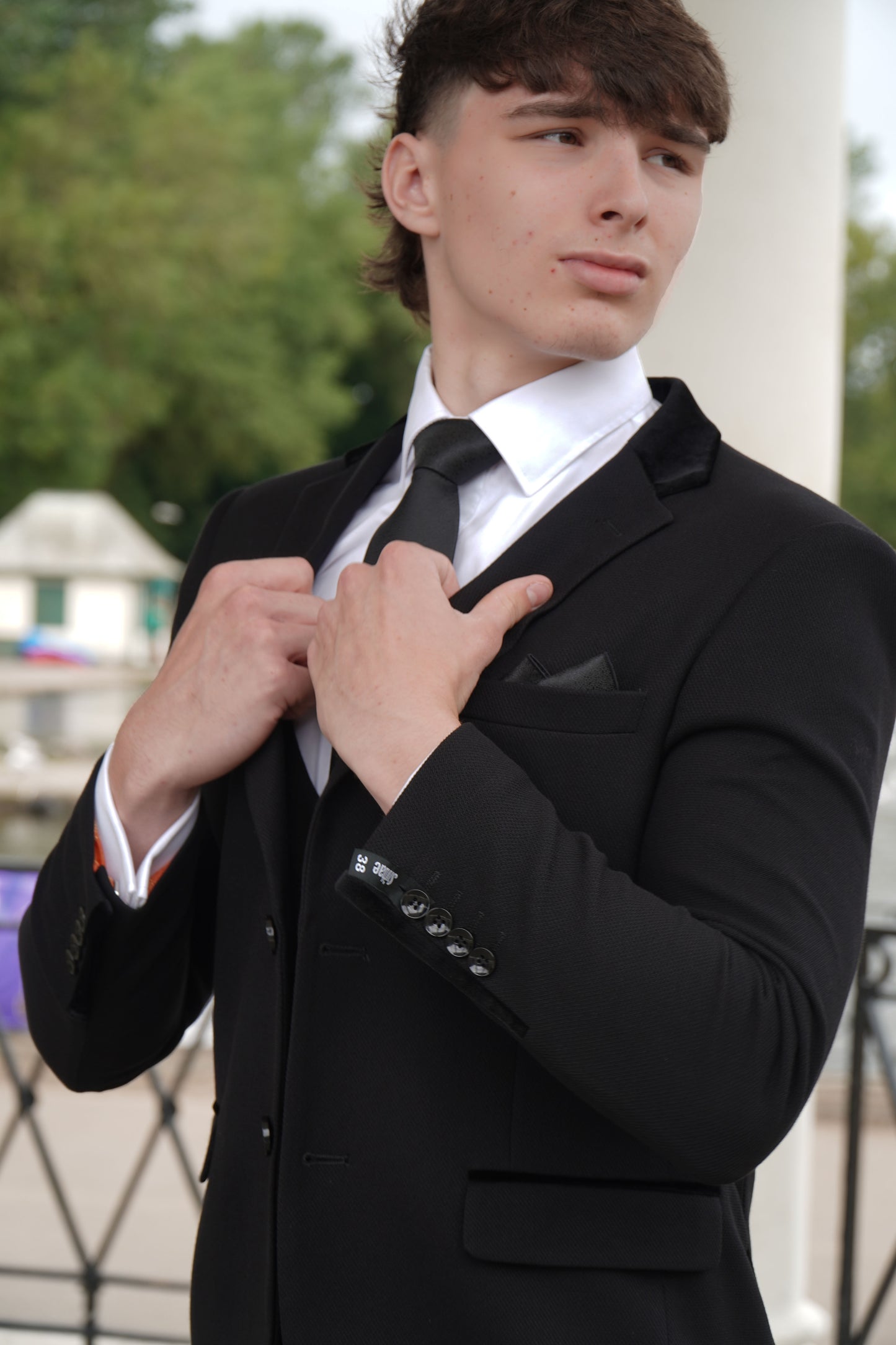 Model wearing the SUITBAE Majid Textured Three-Piece Suit — classic black tailored design with subtle textured fabric, styled with a white shirt and black tie for weddings, proms and formal occasions.