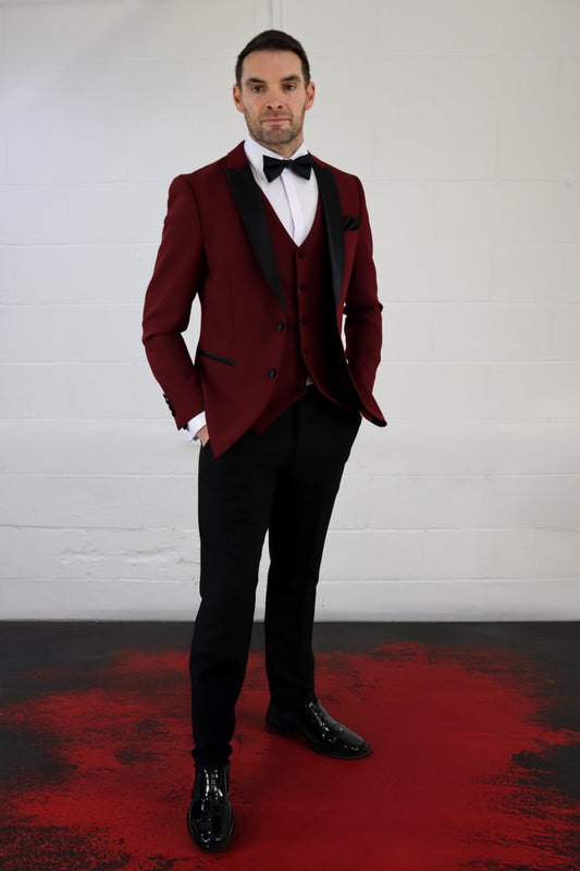 Model wearing the SUITBAE Diablo Blood Red Three Piece Tuxedo featuring black satin lapels, matching waistcoat, and black trousers — perfect for weddings, proms, and formal events.