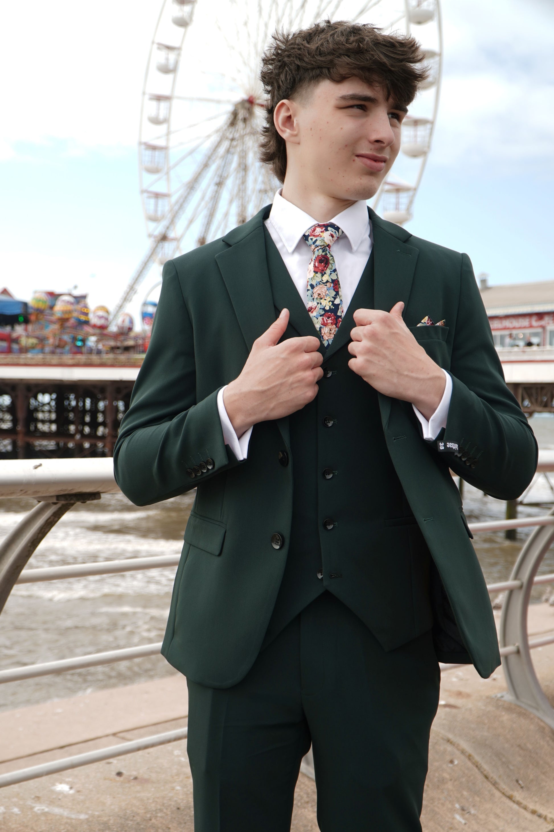 Model wearing the SUITBAE Archie Green Three-Piece Suit — deep green slim-fit design styled with a floral tie and pocket square, perfect for weddings, proms and race day occasions.