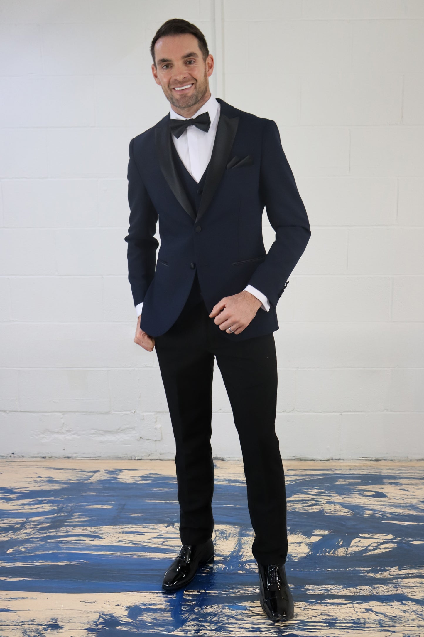 Model wearing the SUITBAE Diablo Navy Three Piece Tuxedo with satin lapels and black bow tie — a sharp navy dinner suit ideal for weddings, proms, and formal black-tie occasions.