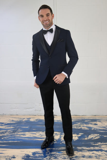 Model wearing the SUITBAE Diablo Navy Three Piece Tuxedo with satin lapels and black bow tie — a sharp navy dinner suit ideal for weddings, proms, and formal black-tie occasions.