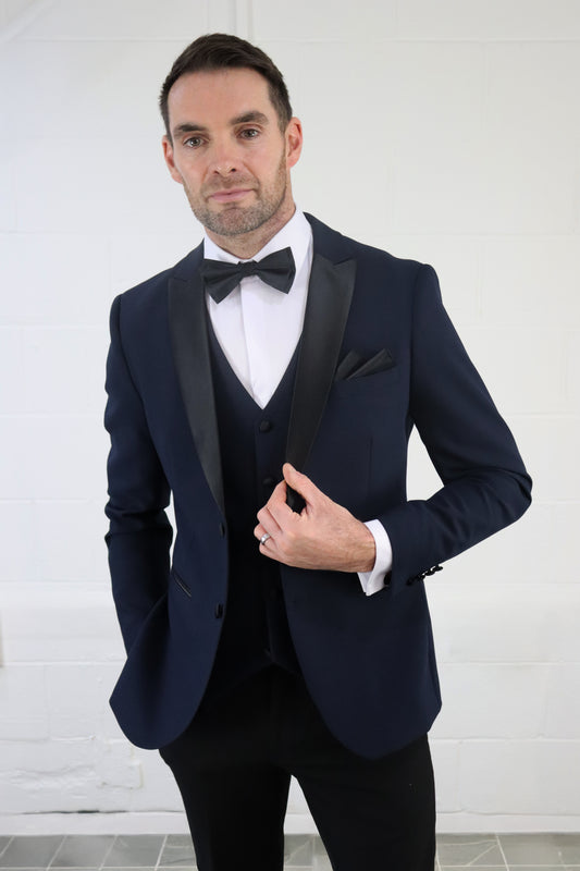 Model wearing the SUITBAE Diablo Navy Three Piece Tuxedo with satin peak lapel, bow tie, and matching waistcoat — perfect for weddings, proms, and black-tie events.