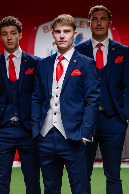 Barnsley FC captain wearing the SUITBAE Charles Navy Contrast Three-Piece Suit with a light grey waistcoat, red tie, and matching pocket square, standing confidently with teammates in matching navy suits and brown brogues inside Oakwell Stadium.