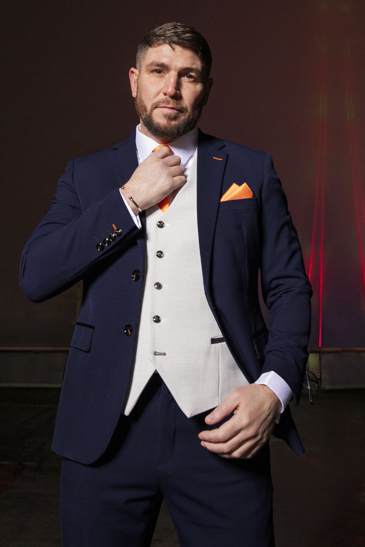 Model wearing the SUITBAE Charles Navy Contrast Three Piece Suit featuring a navy blazer and trousers with a stone waistcoat, paired with an orange tie and pocket square — perfect for weddings or race days.