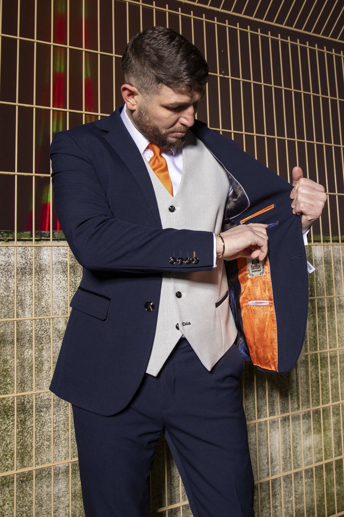 Man wearing the SUITBAE Charles Navy Contrast Three Piece Suit with stone waistcoat and tangerine lining, styled with an orange tie — ideal for weddings, races, or formal occasions.
