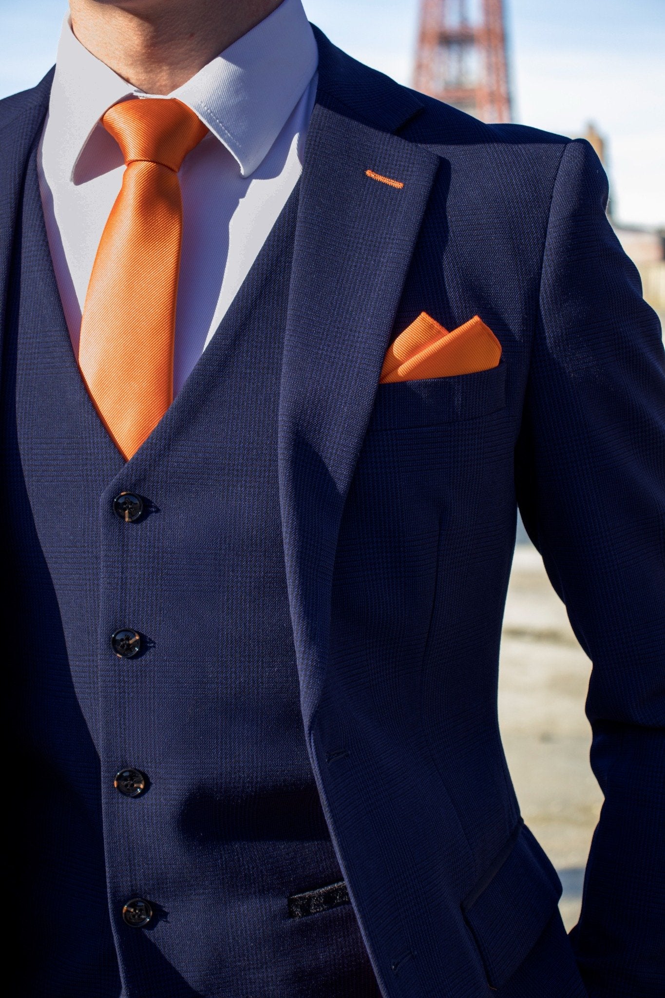 Close-up of the SUITBAE Charles Navy Three-Piece Suit showing the textured navy fabric, notch lapel, and matching waistcoat. Styled with a bold orange tie and pocket square — SUITBAE’s signature tangerine touch — perfect for weddings, races, and formal occasions. Available in plus sizes.
