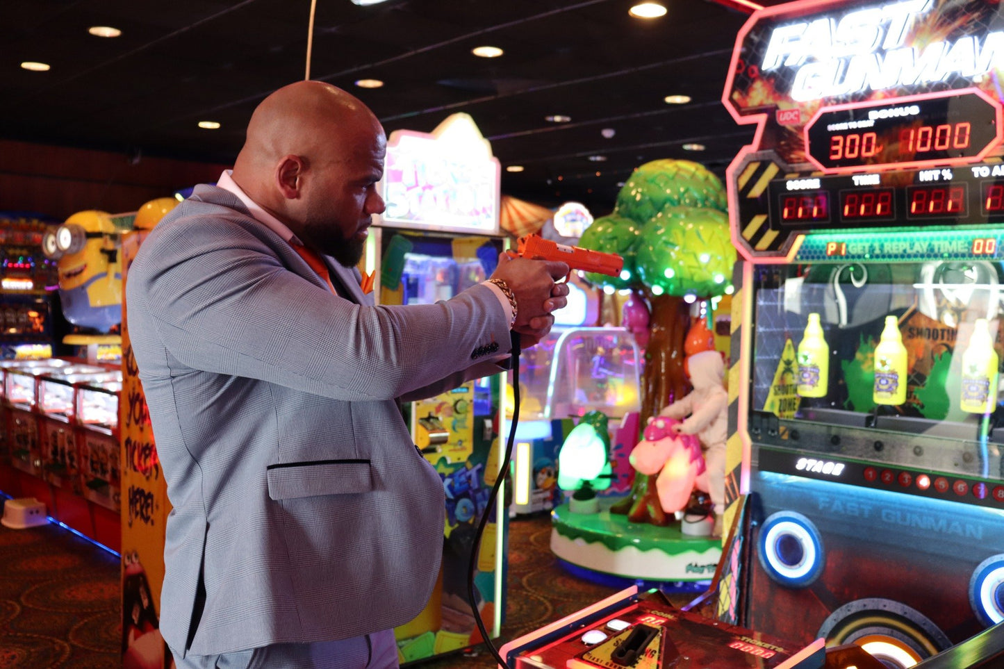 Man wearing the SUITBAE Charles Sky Three-Piece Suit in a light blue check pattern inside a colourful arcade, styled with a tangerine tie and pocket square — a tailored slim-fit men’s suit ideal for weddings, races and proms, available in plus sizes.