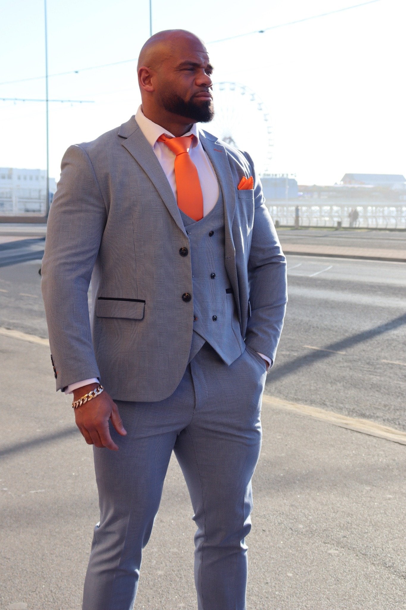 Model wearing the SUITBAE Charles Sky Three-Piece Suit on Blackpool Promenade, featuring a light blue slim-fit blazer, matching waistcoat and trousers, styled with a tangerine tie and pocket square — perfect for weddings, proms and race days, available in plus sizes.