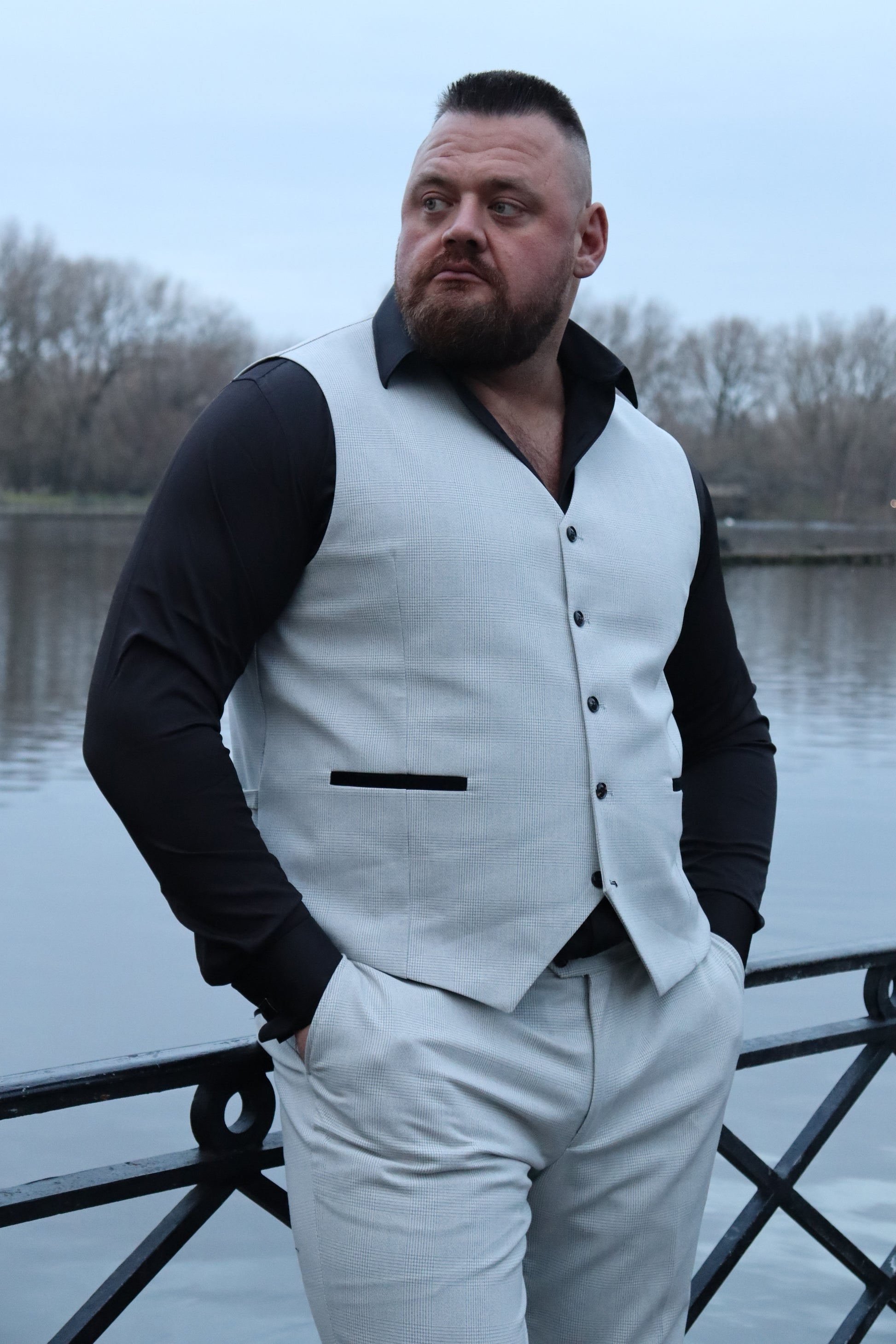 Model wearing the SUITBAE Charles Stone waistcoat and trousers, paired with a black shirt. The light stone fabric and black contrast pockets create a sharp, modern look. Ideal for weddings, proms, or summer events. Available in plus sizes for a perfect tailored fit.