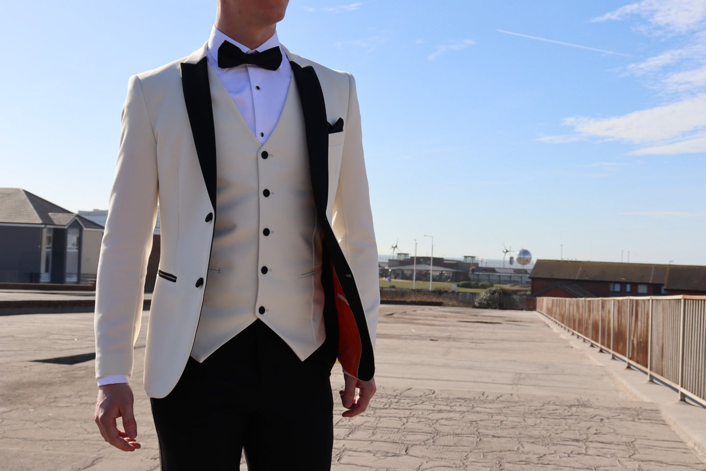 Model wearing the SUITBAE Diablo Ivory Three-Piece Tuxedo featuring a black satin peak lapel blazer, ivory waistcoat, and black trousers — luxury tuxedo ideal for weddings, proms and black-tie events, available in plus sizes.