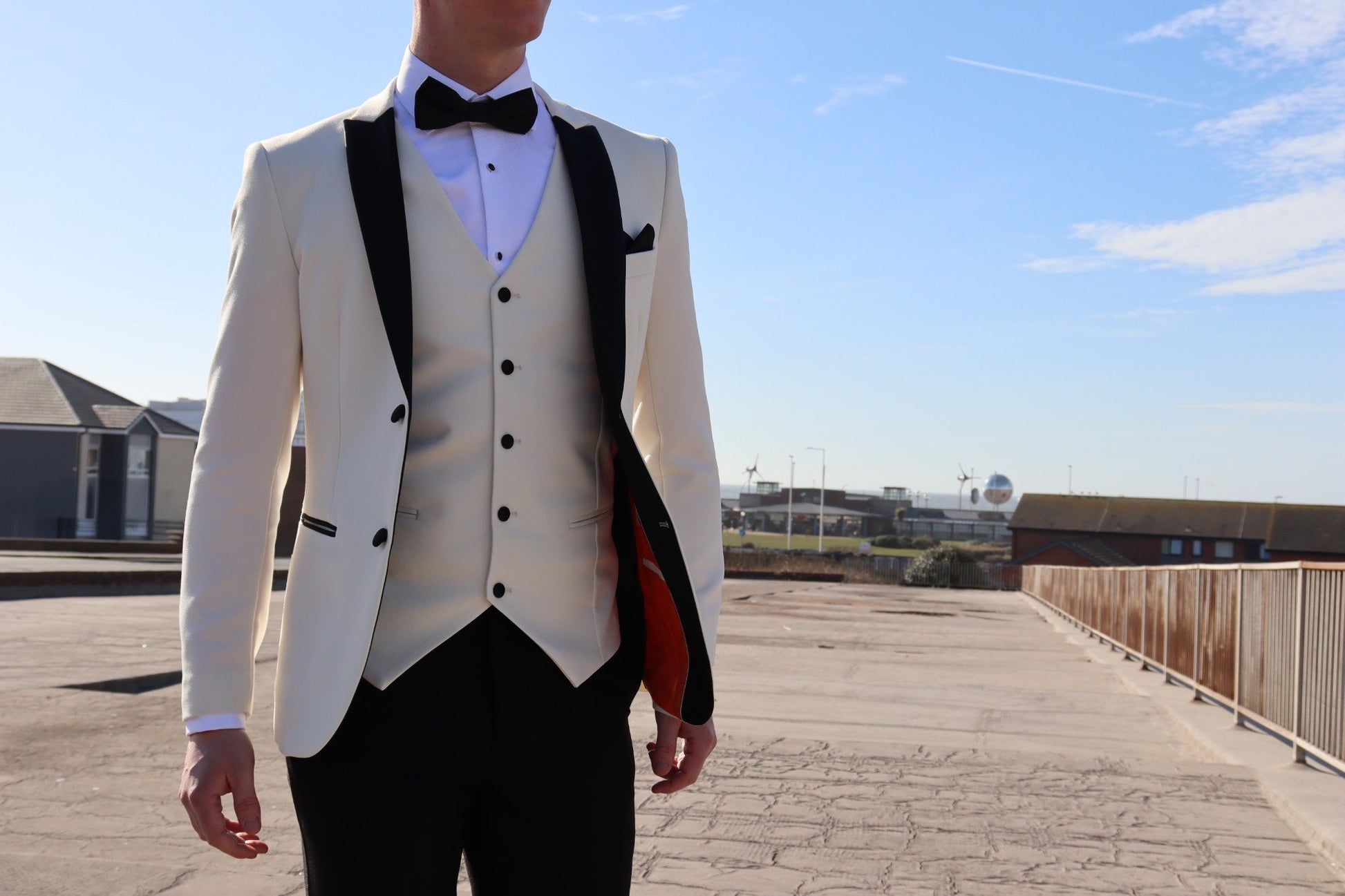 Model wearing the SUITBAE Diablo Ivory Three-Piece Tuxedo featuring a black satin peak lapel blazer, ivory waistcoat, and black trousers — luxury tuxedo ideal for weddings, proms and black-tie events, available in plus sizes.