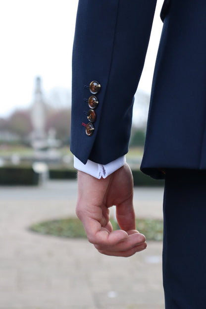 Close-up of a man’s arm wearing a navy suit jacket with brown buttons and visible white shirt cuff, showing the sleeve detail and stitching from the SUITBAE collection.