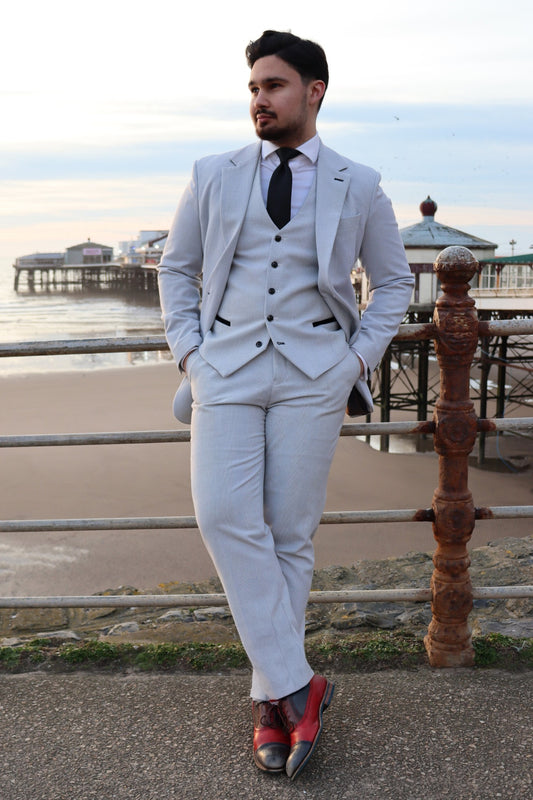 Model wearing the SUITBAE Charles Stone Three-Piece Suit in light stone grey with a black tie, posing by Blackpool pier — ideal for weddings, races, and prom season.