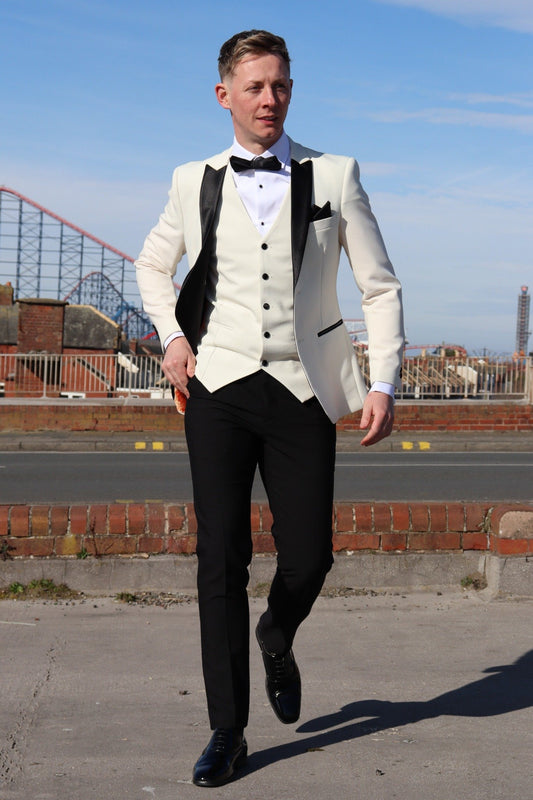 Model walking in the SUITBAE Diablo Ivory Three-Piece Tuxedo with black trousers and satin peak lapels — a sharp men’s tuxedo ideal for weddings, proms and formal black-tie occasions.