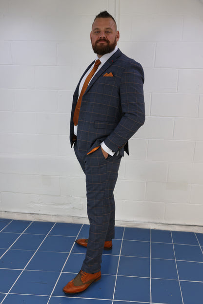 Man wearing the SUITBAE Thomas Check Two Piece Suit in navy with bold textured pattern, styled with a white shirt, burnt orange tie and pocket square. Ideal for weddings, races, or standout formal events.